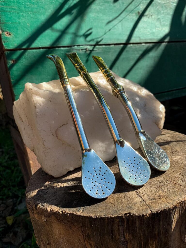 Set de tres bombillas doradas de acero inoxidable con diferentes diseños, apoyadas sobre piedra blanca, fotografía artesanal.