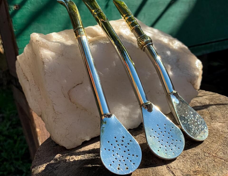 Set de tres bombillas doradas de acero inoxidable con diferentes diseños, apoyadas sobre piedra blanca, fotografía artesanal.